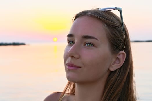 Portrait of a young beautiful girl in the sunrise light, with water in the background.