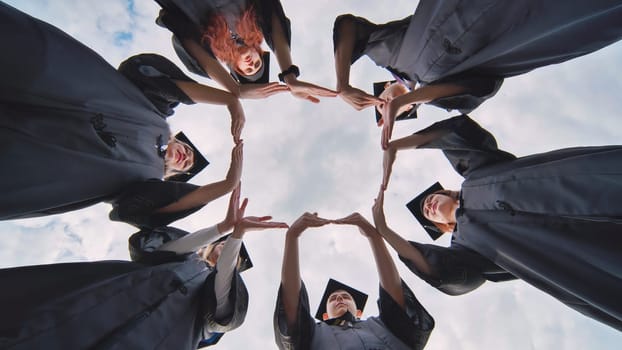 College graduates in black robes make the shape of a square from their hands