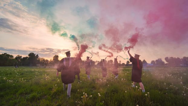 Graduates in costume walk with a smoky multi-colored smoke at sunset