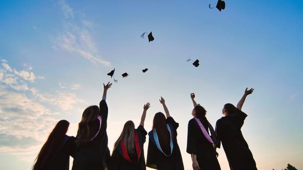 Silhouettes of graduates toss their caps at sunset