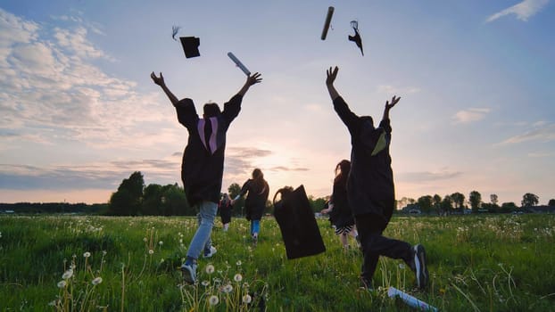 College graduates run to meet the sun and toss their caps and diplomas