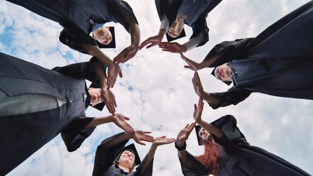 Graduate students in black robes and caps make a circle shape from their hands