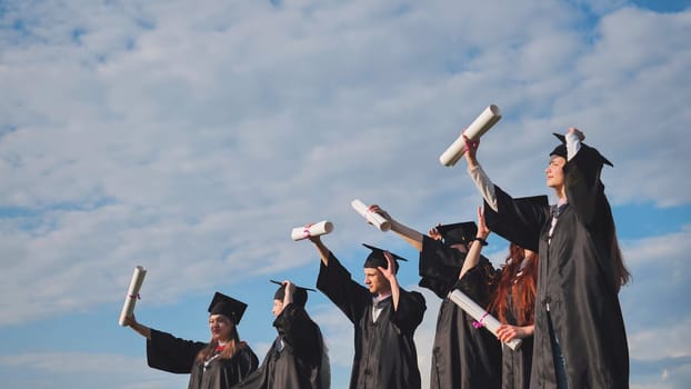 Cheerful graduates pose with raised diplomas on a sunny day