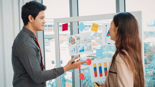 Business people work on project planning board in office and having conversation with coworker friend to analyze project development . They use sticky notes posted on glass to make it organized. Jivy