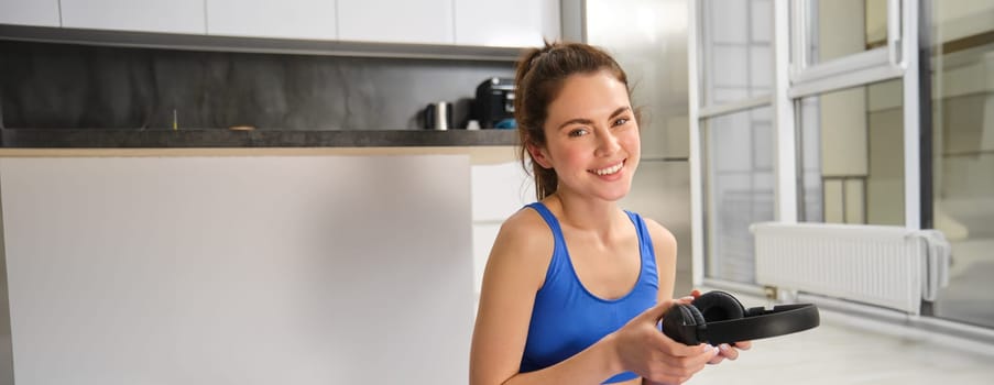 Portrait of woman doing home fitness exercises on yoga mat, listening music in wireless headphones, focusing on workout in earphones.