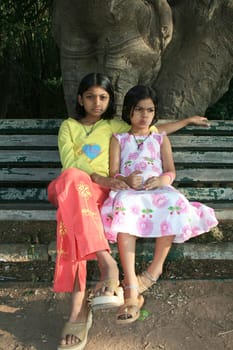Two sisters in thoughtful mood sitting on a park bench