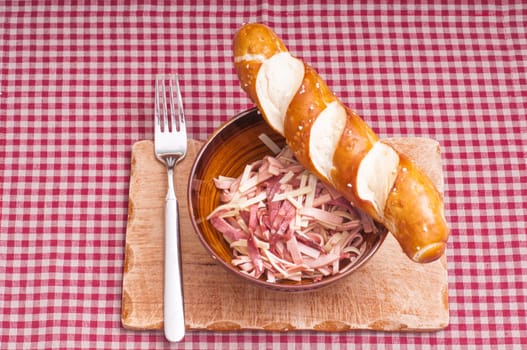 Sausage salad with cheese and pretzel stick on a wooden board and red checkered tablecloth