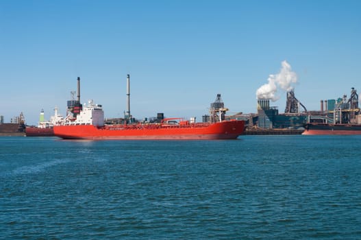 red tanker passing by a large steel factory in IJmuiden, Netherlands