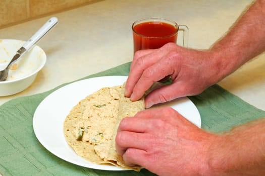 Male hands rolling up salmon salad with jalapenos in a multi-grain soft tortilla for lunch.