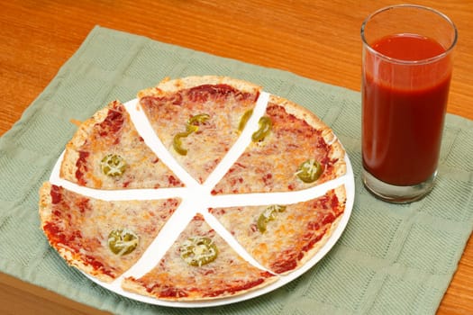 Sliced thin crust tortilla pizza topped with tomato paste, mozzarella cheese, jalapenos and pepper along with a tall glass of tomato vegetable juice.