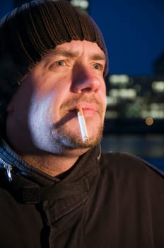Head portrait of a middle-aged man with woolen hat and cigarette to the side and looking up