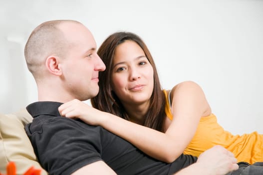 Upper body portrait of a young couple at home lying arm in arm on the couch with a single flower lying in front of it on the table