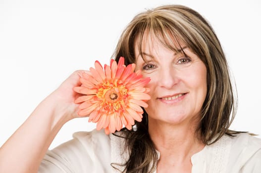 Head and shoulders portrait of a middle-aged woman with orange-colored flower against neutral light studio background