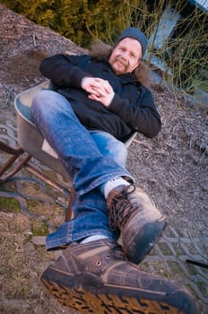 Full length portrait of an elderly man resting in a wheelbarrow and smiling looking at the camera