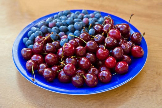 Blueberries and cherries lay on blue painted plate