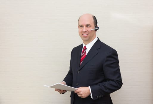 Business man with a handsfree telephone headset holding a document.