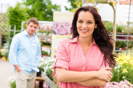Smiling woman posing at garden centre young man in background