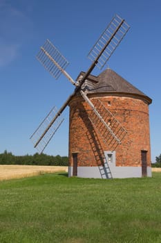 Brick windmill in a field of corn and the green grass.. Blue sky in the background. (Chvalkovice, Czech Republic)