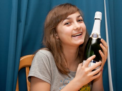 Girl with bottle champaign smiles on turn blue background