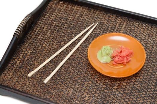 Orange saucer with ginger and sharp seasoning on bamboo tray near by chopstick insulated on white background