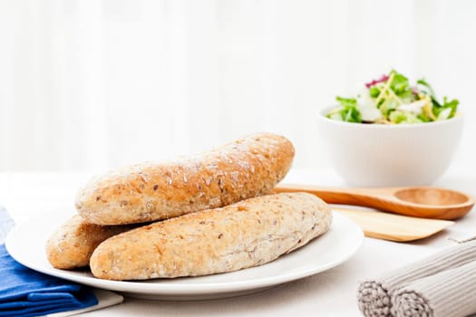 Three bread rolls on the dinner table with salad in the background.
