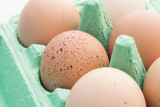 Brown eggs in green packaging, one speckled.
