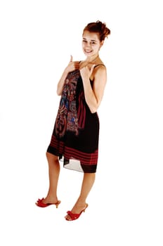 A pretty girl in a black colorful dress and high heels standing for white background holding her thumps up for good luck.