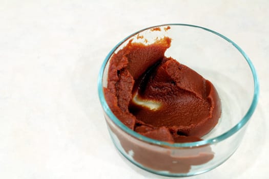 Organic tomato paste in a small clear glass bowl on a kitchen counter.