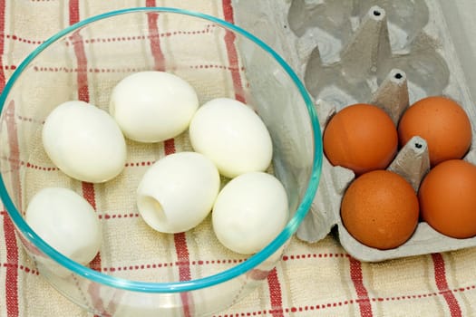 Six boiled eggs in a glass bowl next to four organic brown eggs in an egg carton.