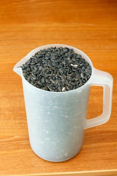 Black oil sunflower seeds in a plastic pitcher used to refill bird feeders.
