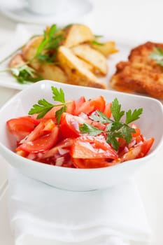 Tomato salad with onion and potatoes wedges in background