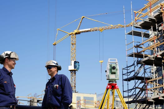 two building workers, engineers with surveying measuring instrument