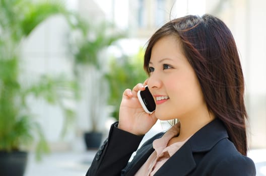 Young Asian business woman talking phone outside modern building