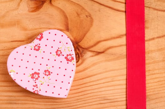 Pink heart with flowers and red ribbon on a wooden board