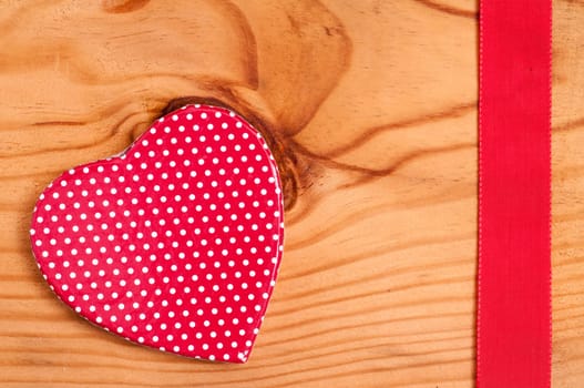 Red heart with white dots and red ribbon on a wooden board