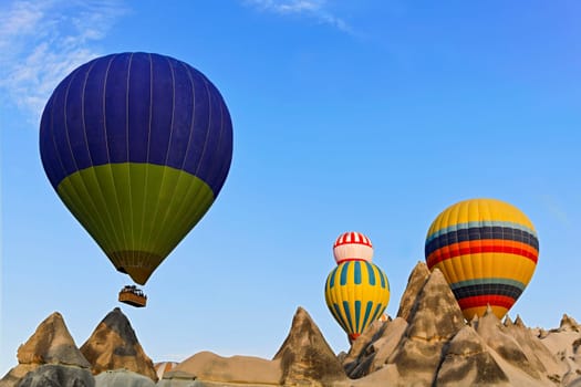 Hot air balloons captured coming over the limestone ridge near Goreme, Caapadocia, Turkey. The weathered mineral peaks which have eroded through evolution present a surrel backdrop to the striking colours of the passenger ladened aircraft.