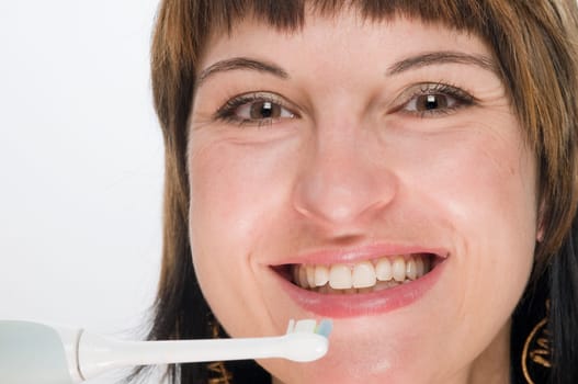 Frontal head shot of young brunette woman with electric toothbrush smiling looking at camera against white background