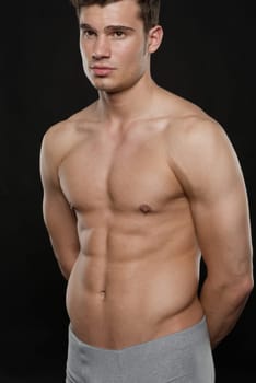 Young shirtless man against black studio background