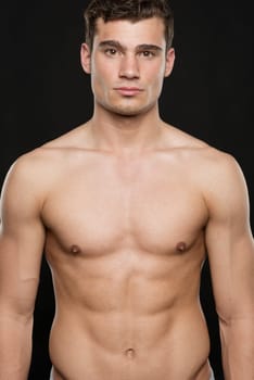 Young shirtless man against black studio background