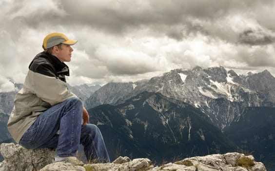 Young man sitting at the summit and enjoying the view of the mountain landscape