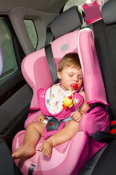 Infant baby sleeps peacefully secured with seat belts while in the car.