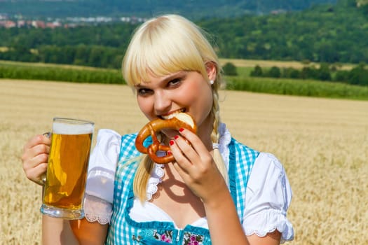 Young woman in dirndl with pretzel and beer