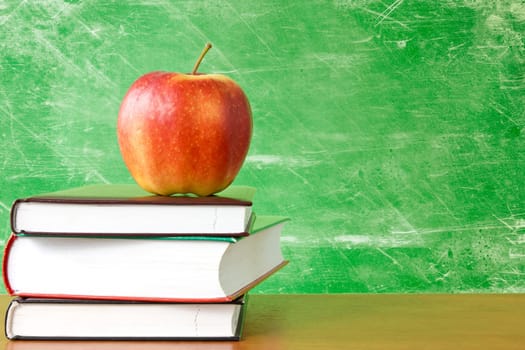 red apple on a pile of books against dirty chalkboard
