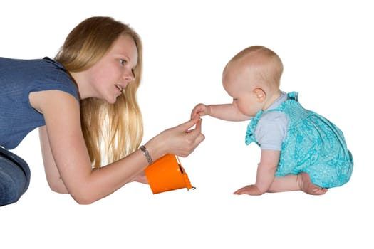 Young mother kneeling on the floor giving a treat to her adorable small baby who is carefully taking it from her hand