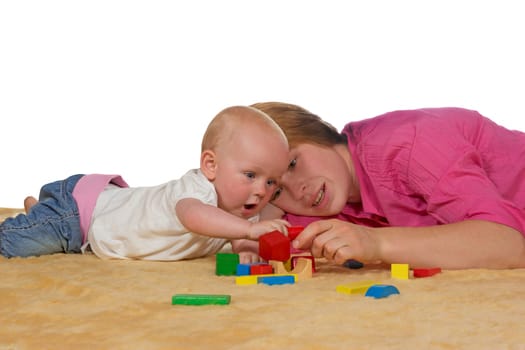 Mum and her small baby lying close together on the floor playing with building blocks as she teaches it coordination and shapes