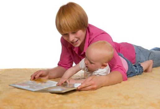 Mother lying on the floor with her arm protectively around her cute young baby looking at a book together