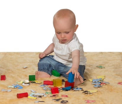 Adorable young baby sitting contentedly on the floor playing with an assortment of educational toys