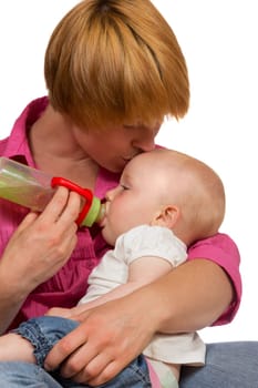Young Mum bottlefeeding her adorable small baby cradled in her arms as she kisses it lovingly on the forehead