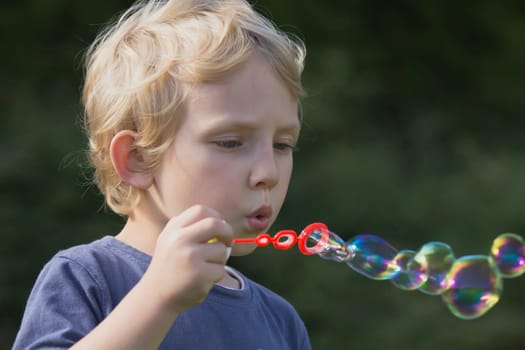 Side view of a blond boy who blows soap bubbles.
