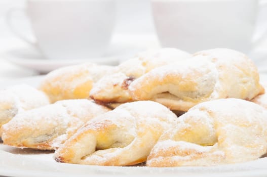 Closeup of homemade jam filled crescent rolls and white cups of tea